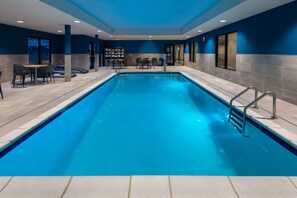 A swimming pool with a tiled deck, a seating area with tables and chairs, and a blue wall. - Hampton Inn & Suites Cody (Cody)