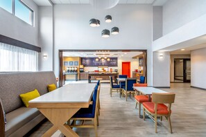 A modern dining area with a long table, several chairs, and a sofa. There are ceiling lights and a visible kitchen area in the background. - Hampton Inn & Suites Cody (Cody)