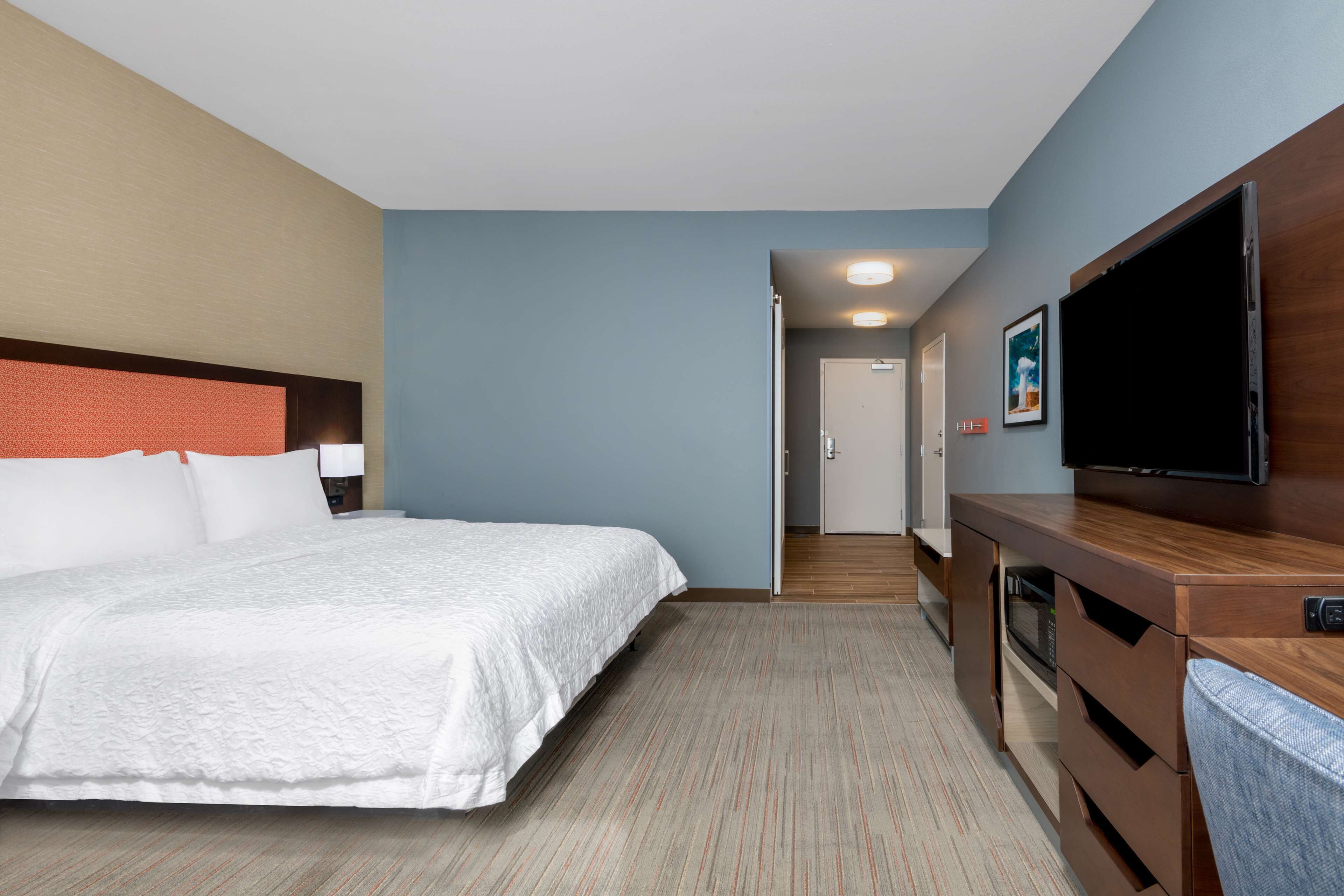 Une chambre d’hôtel avec un grand lit, un téléviseur à écran plat, une commode en bois et une porte donnant sur une autre pièce.