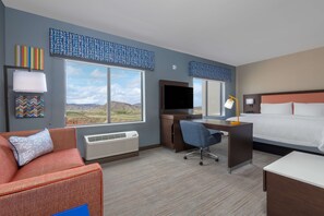 A hotel room with a large window, a desk, a bed, and a couch. - Hampton Inn & Suites Cody (Cody)