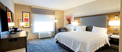 A hotel room with a large bed, a desk, a chair, and a TV.