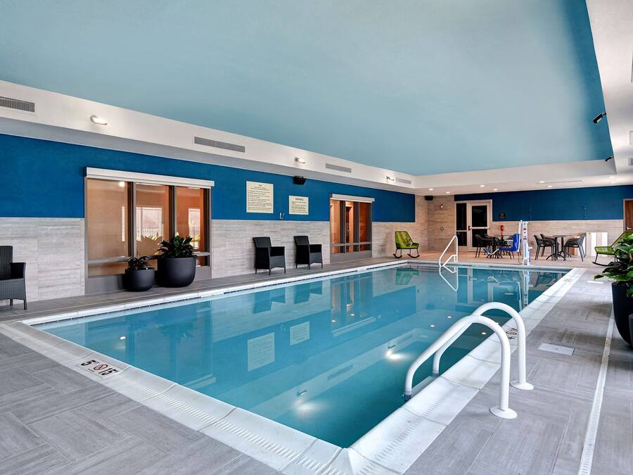 An indoor swimming pool with clear water, surrounded by lounge chairs and potted plants.