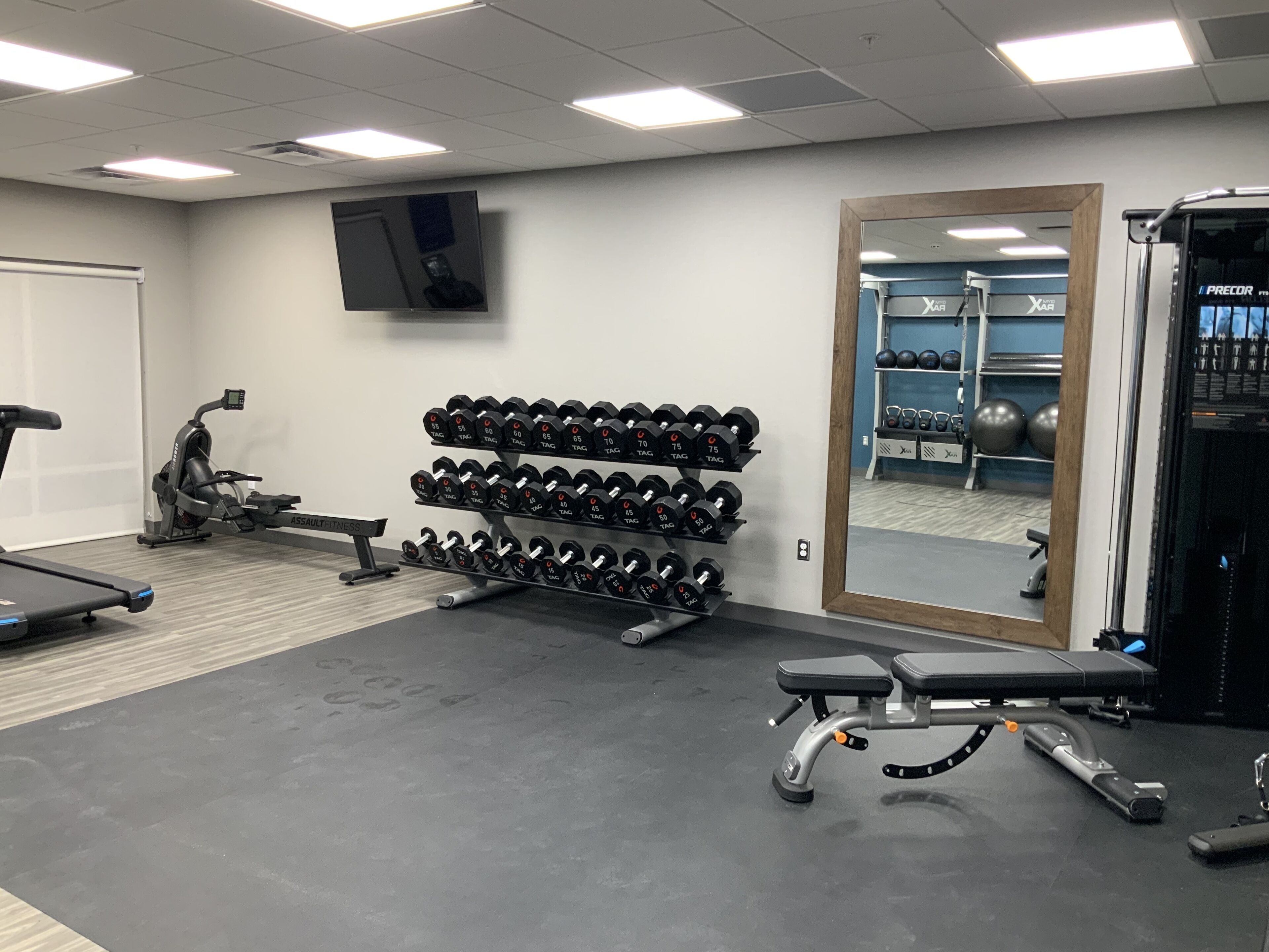 Un gimnasio con equipo de ejercicio, incluyendo mancuernas, una cinta de correr y una banca.