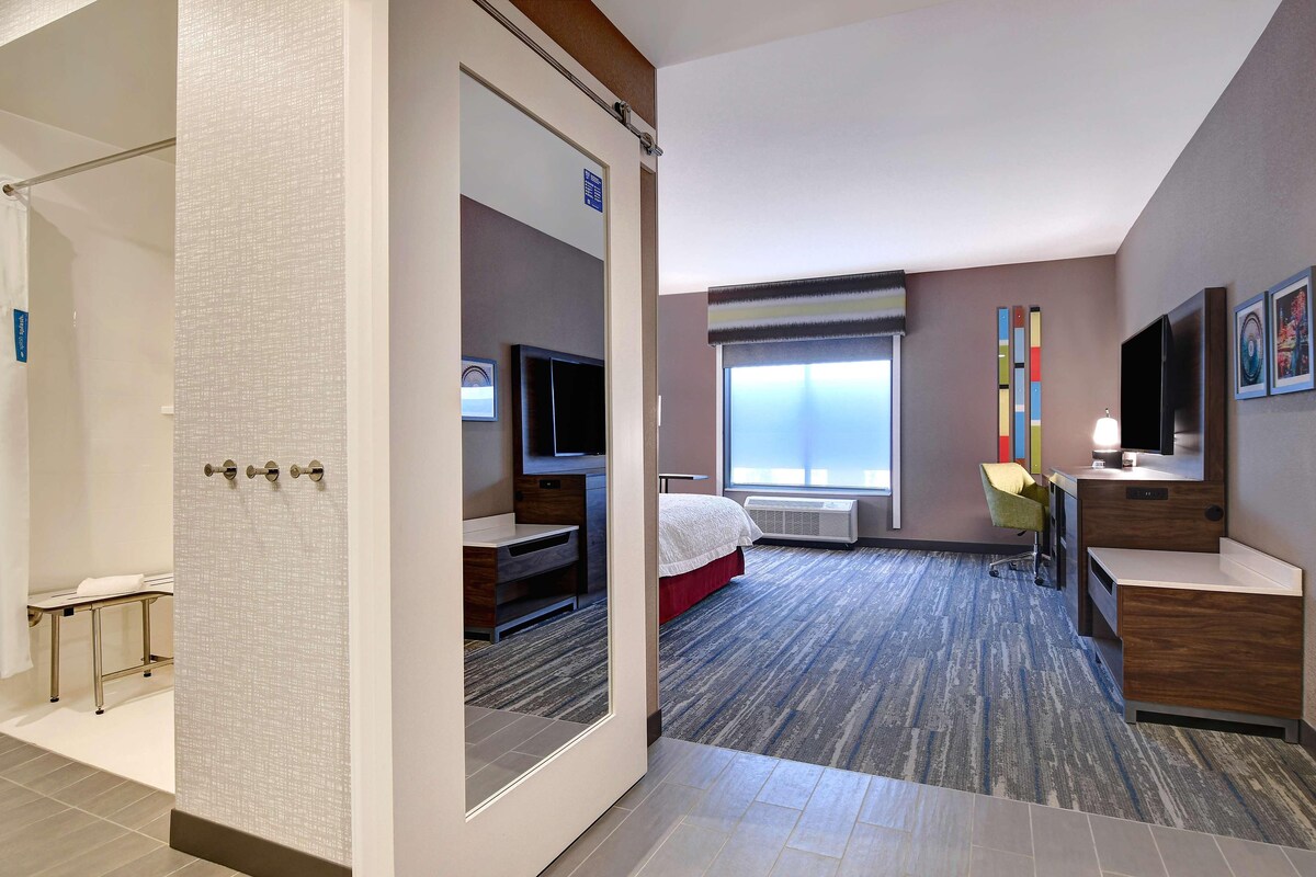 A hotel room with a bed, a desk, a TV, a chair, and a window with blinds.