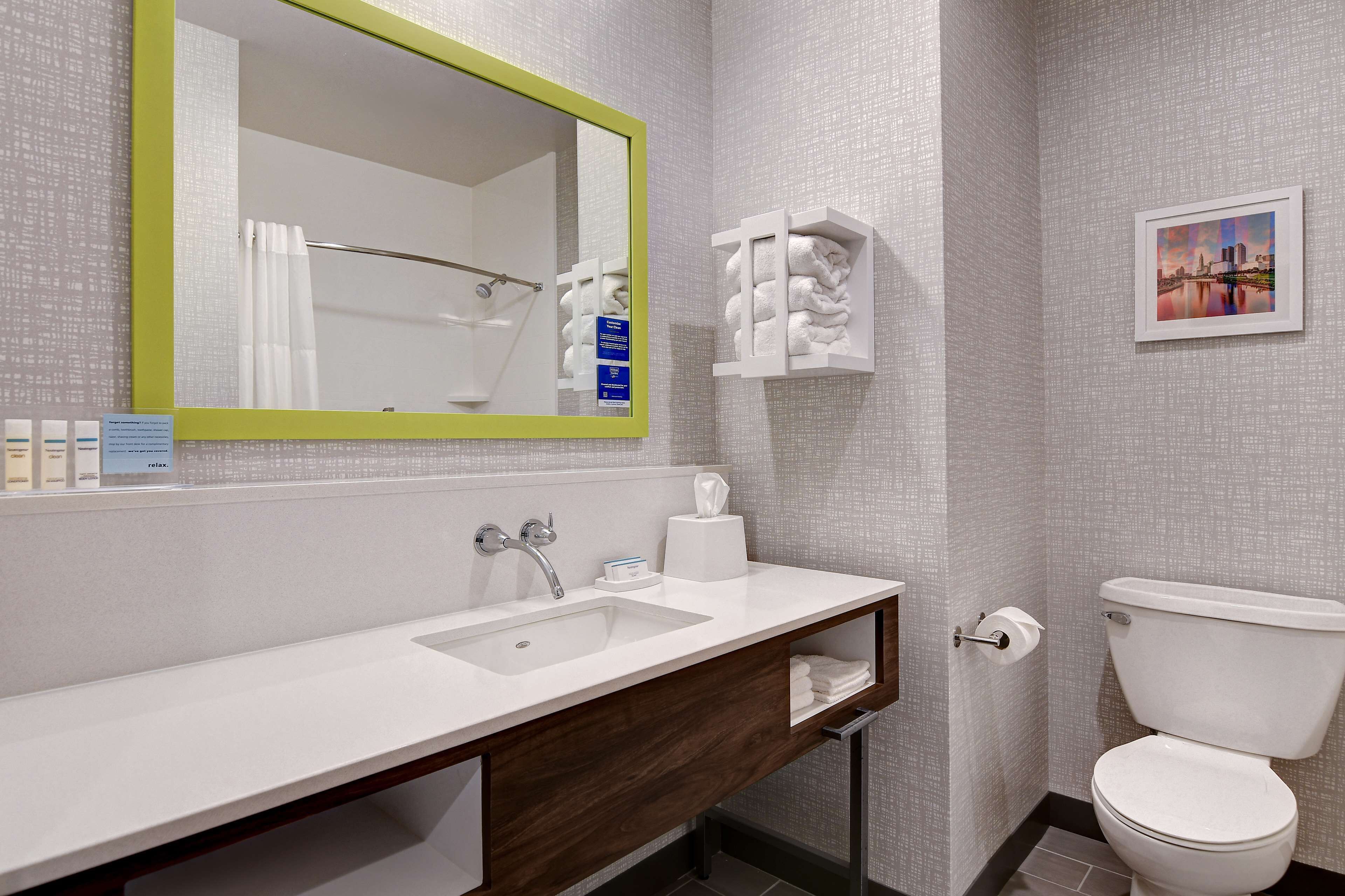 A bathroom with a white sink, a mirror with a green frame, a toilet, and a towel rack.