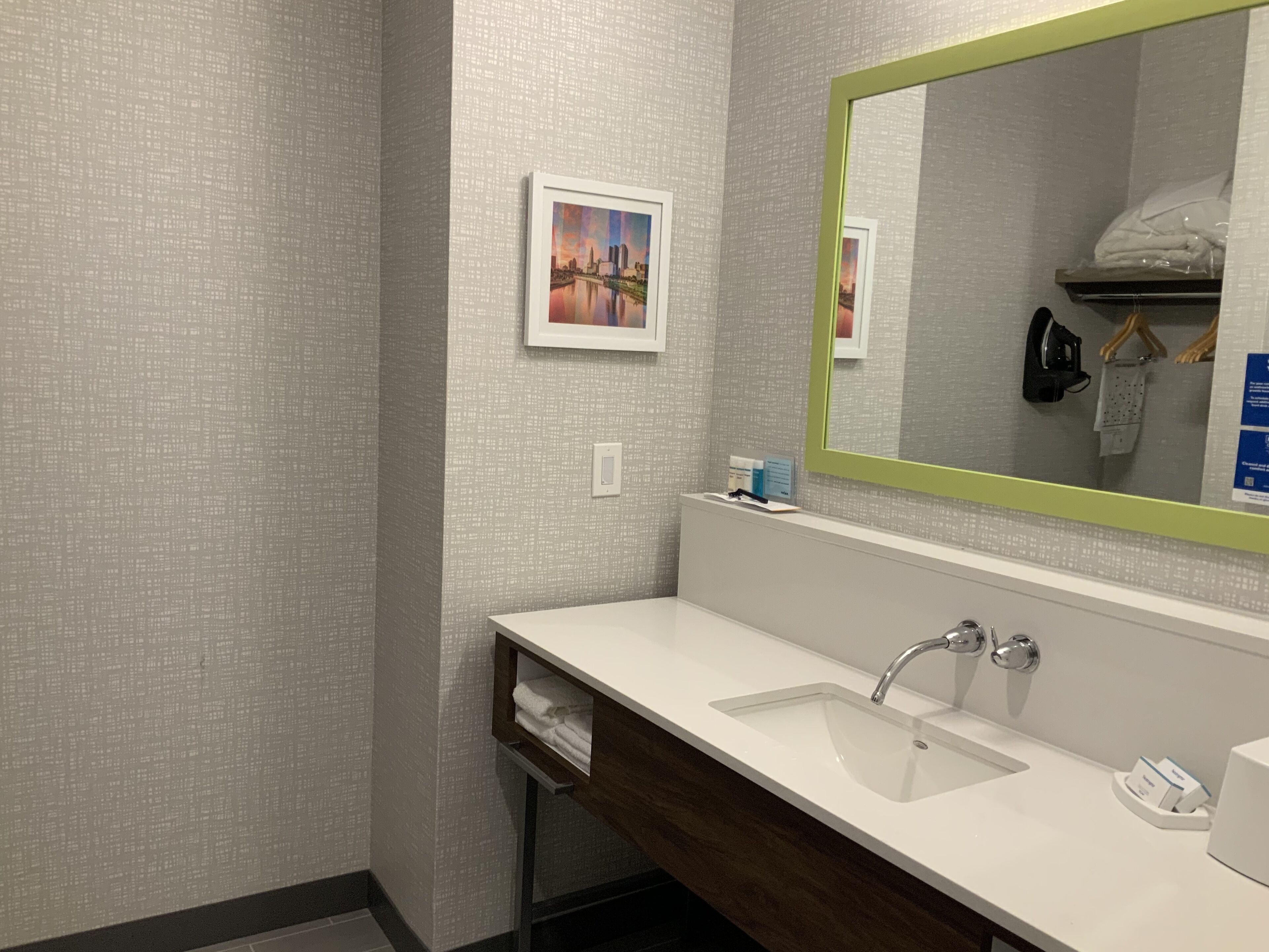 A modern bathroom with a white sink, a large mirror with a green frame, and a small framed picture on the wall.