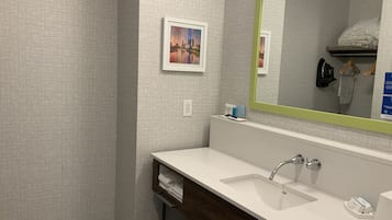 A modern bathroom with a white sink, a large mirror with a green frame, and a small framed picture on the wall.
