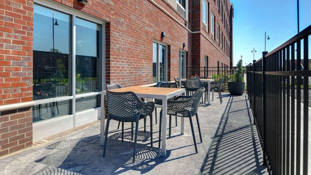 A brick building with large windows, outdoor seating with metal chairs, and a black metal fence. - Hampton Inn & Suites Canal Winchester Columbus (Canal Winchester)