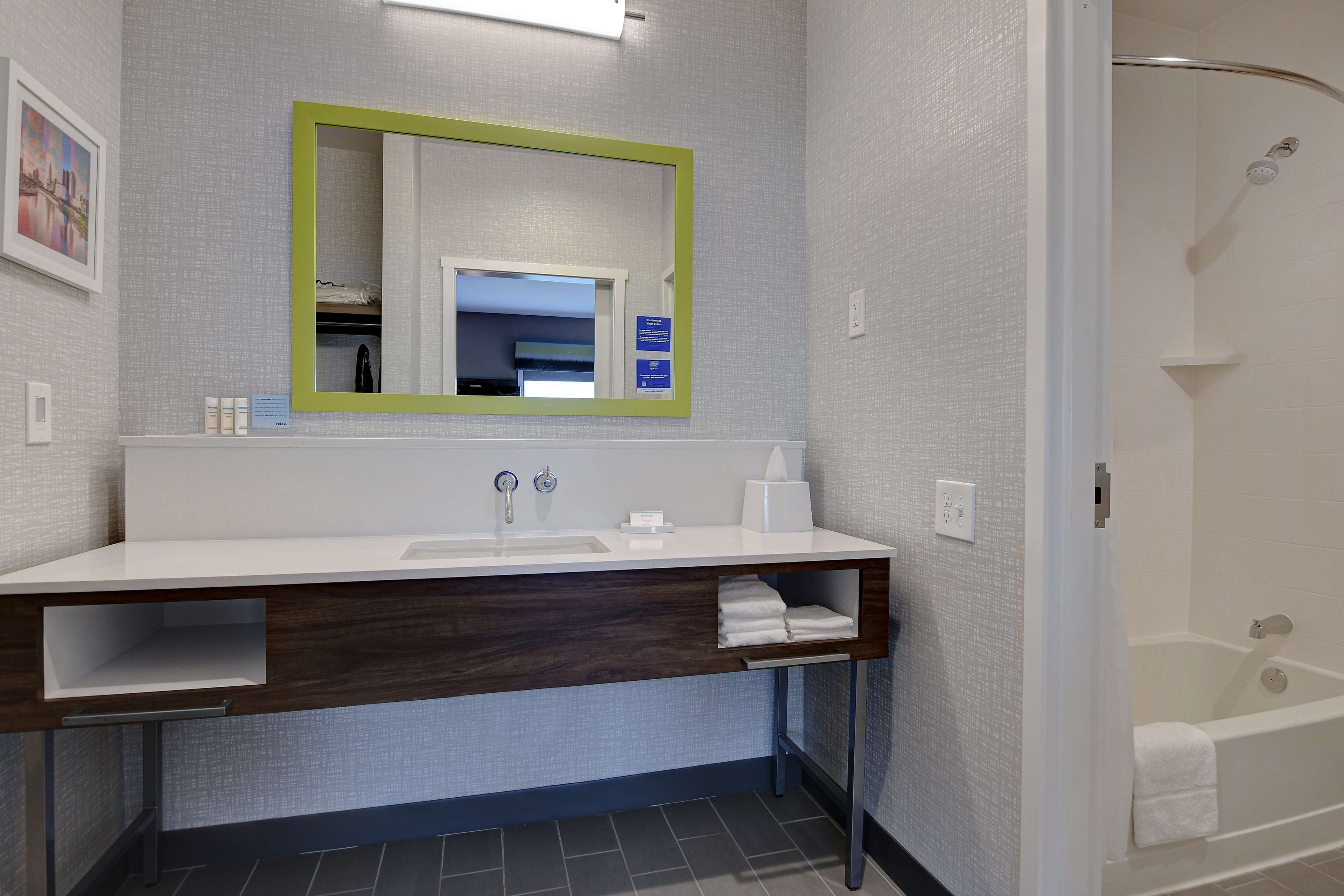 A modern bathroom with a white sink, a mirror with a green frame, a towel rack, and a shower area.