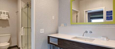Een moderne badkamer met een glazen douche, een witte wastafel en een spiegel met een groene lijst.