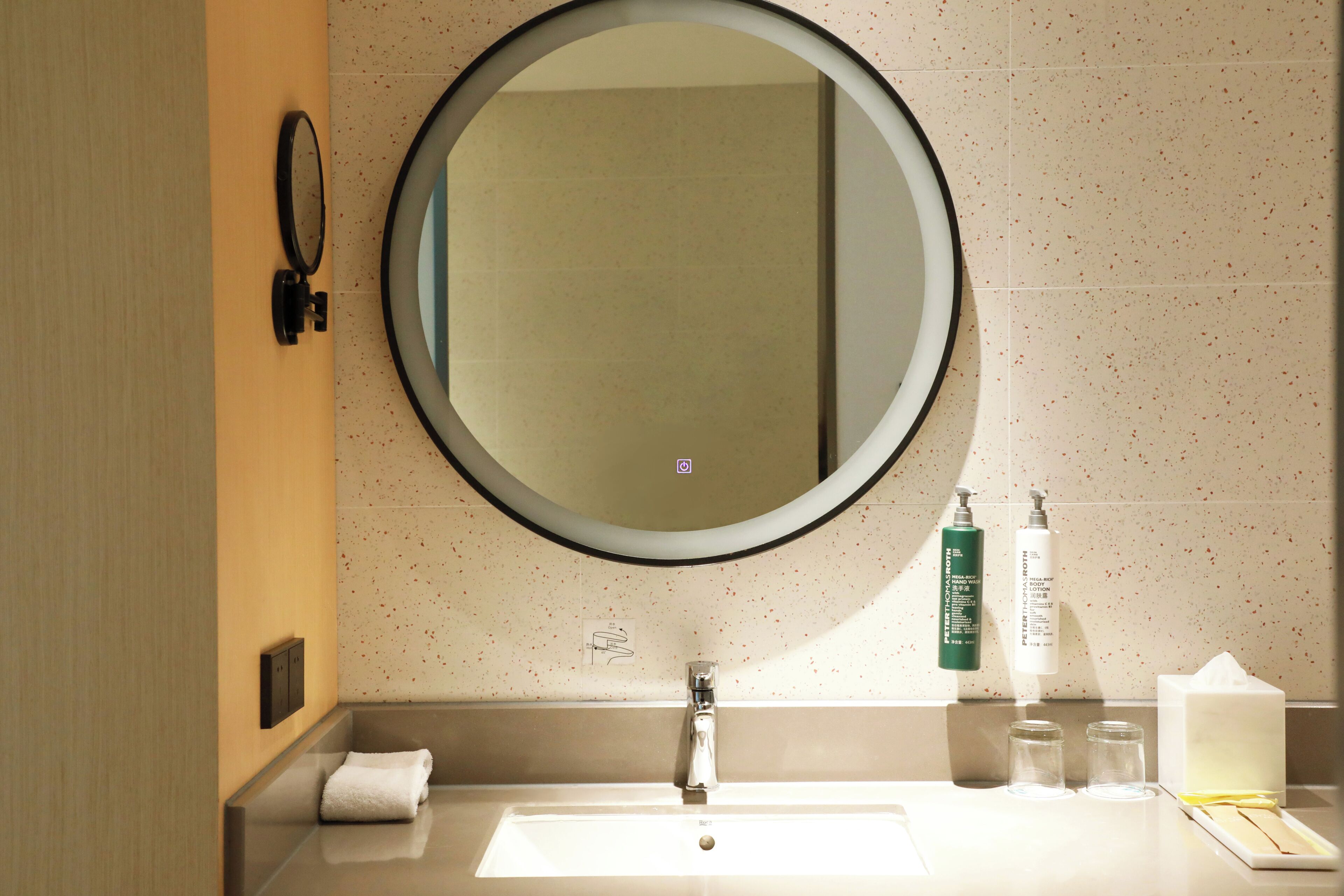 A bathroom with a round mirror, a sink, a towel, and toiletries.