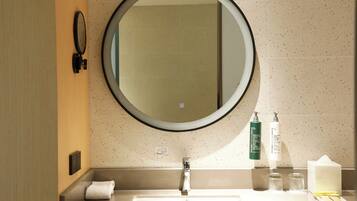 A bathroom with a round mirror, a sink, a towel, and toiletries.