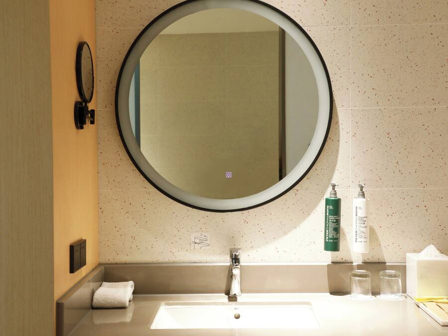 A bathroom with a round mirror, a sink, a towel, and toiletries.