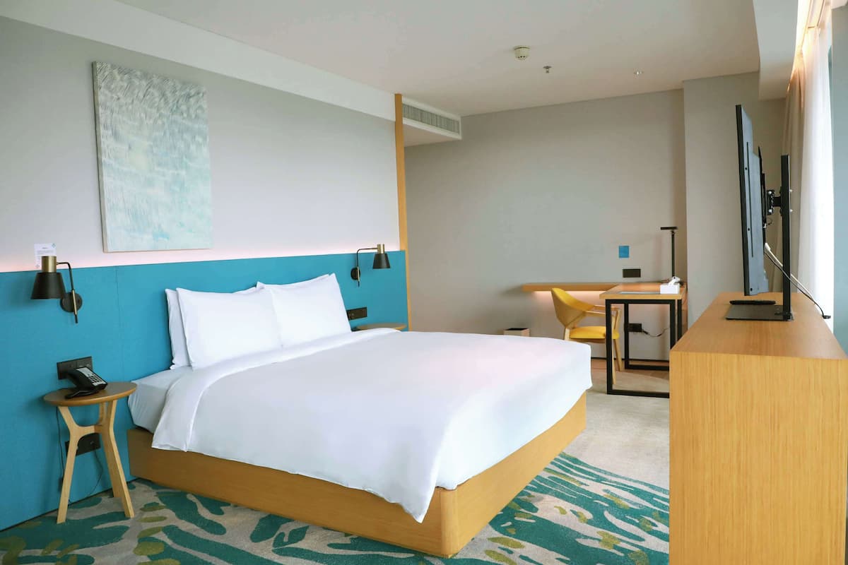 A hotel room with a bed, a desk, a chair, a lamp, and a television.
