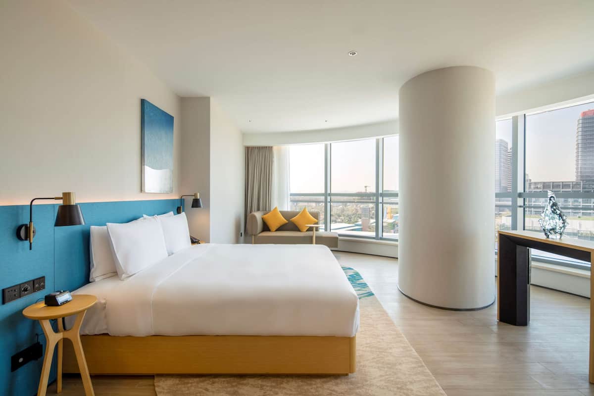 A modern hotel room with a large bed, a desk, and a view of the cityscape.