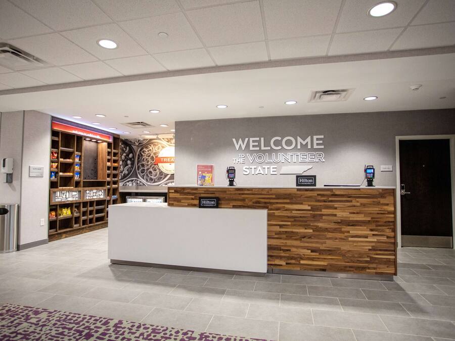 Un'area reception con un cartello 'Welcome to the Volunteer State', una scrivania reception in legno, un banco snack e un cartello 'Hilton Honors'.