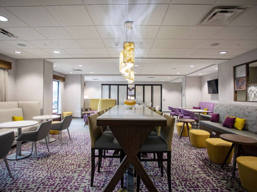A modern hotel lobby with a long dining table, comfortable seating, and a patterned carpet.