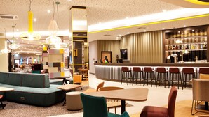 A modern lounge area with seating arrangements, a bar, and a television screen.
