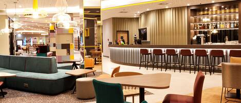 A modern lounge area with seating arrangements, a bar, and a television screen.