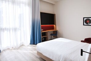 Une chambre d’hôtel moderne avec un grand lit, un bureau avec une chaise, un téléviseur à écran plat et un disque vinyle encadré accroché au mur.