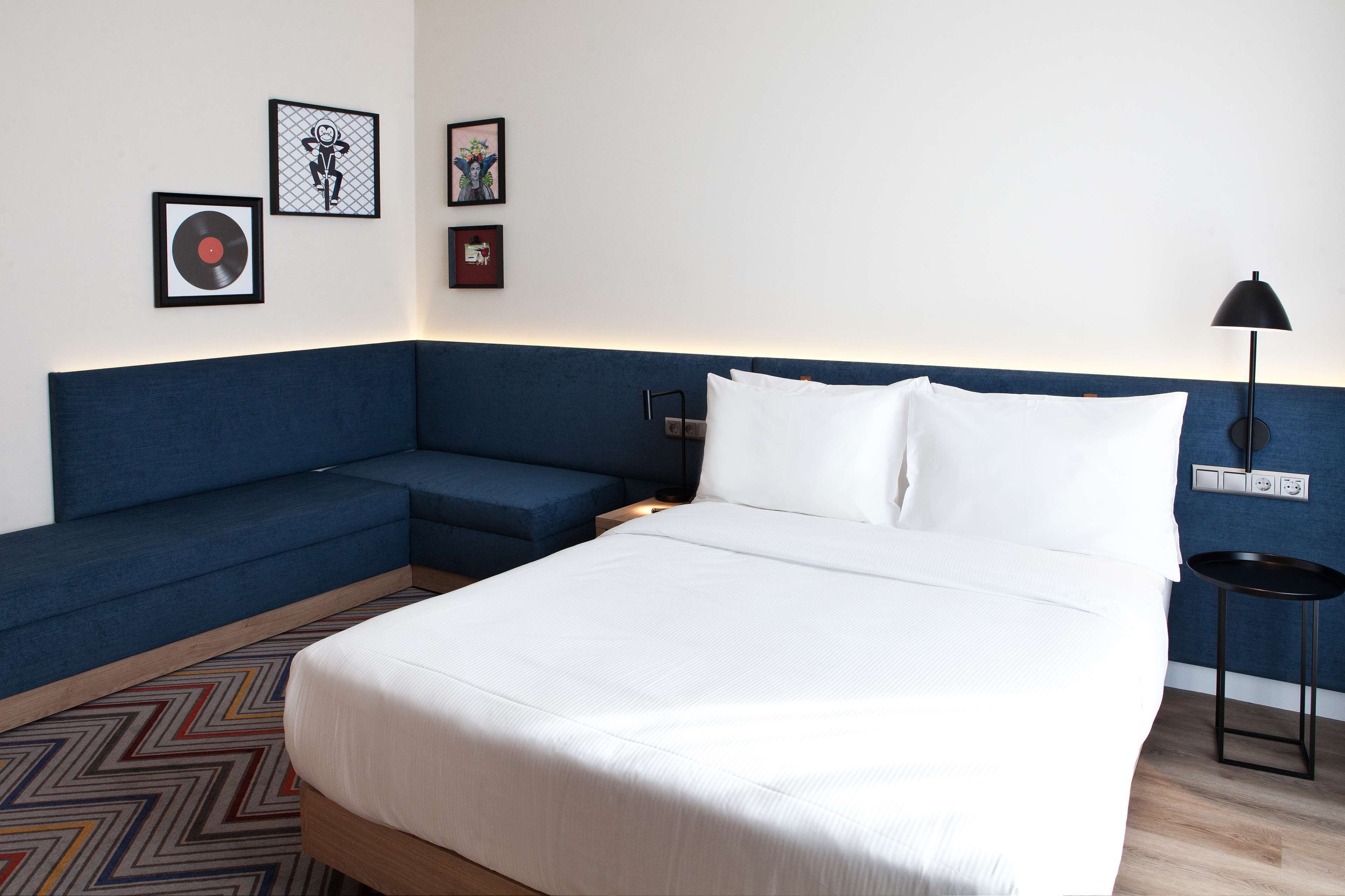 Habitación de hotel con una cama, un sofá azul y una pequeña mesa. Hay cuadros en la pared.
