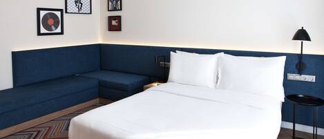 Habitación de hotel con una cama, un sofá azul y una pequeña mesa. Hay cuadros en la pared.