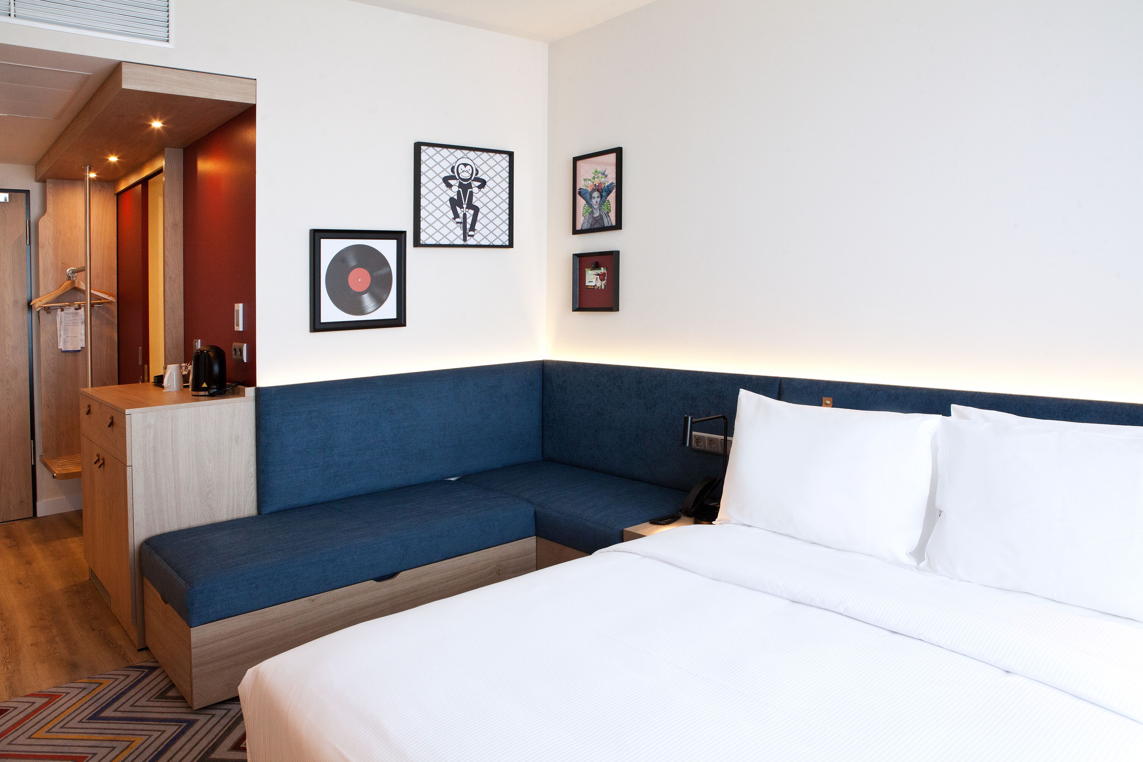 A modern hotel room with a blue sofa, a bed with white linens, and artwork on the walls.