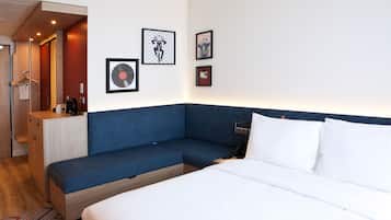 A modern hotel room with a blue sofa, a bed with white linens, and artwork on the walls.