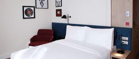 Una habitación de hotel con una cama, una silla roja, una mesita de noche con lámpara y decoración en la pared.