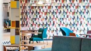 A modern lounge area with a colorful geometric wall, comfortable seating, and stylish pendant lighting.