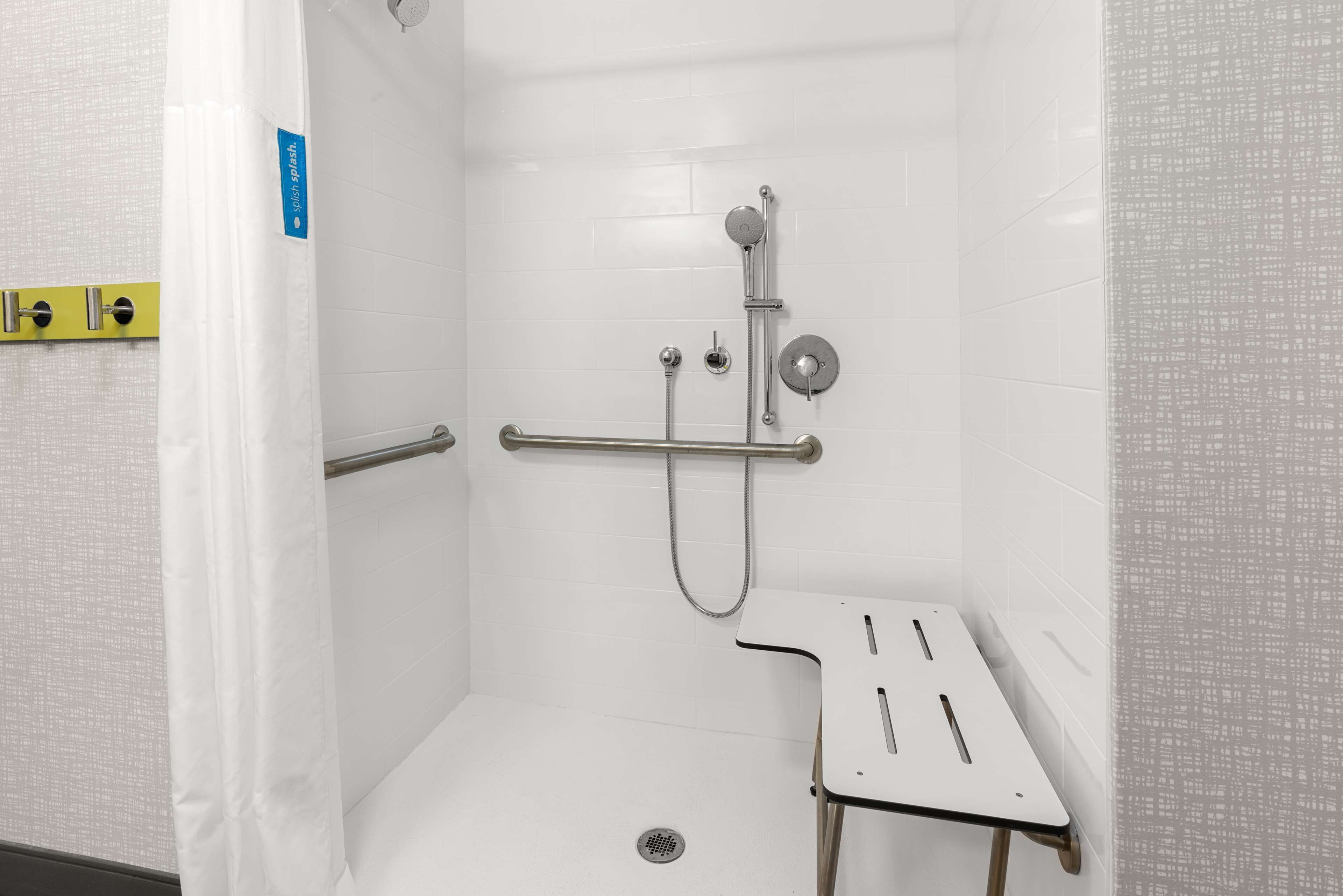 A small, white, tiled shower stall with a handheld showerhead, a handheld shower attachment, and a grab bar.
