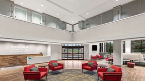 A spacious lobby with a high ceiling, a reception desk, multiple seating areas, and a large window offering a view of the outdoors.