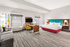 Quarto de hotel com uma cama, escrivaninha, cadeira, televisão e janela.
