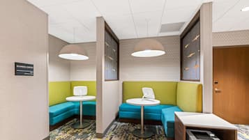 A business center with a 24-hour service sign, two blue sofas, two white tables, and a printer on the floor.