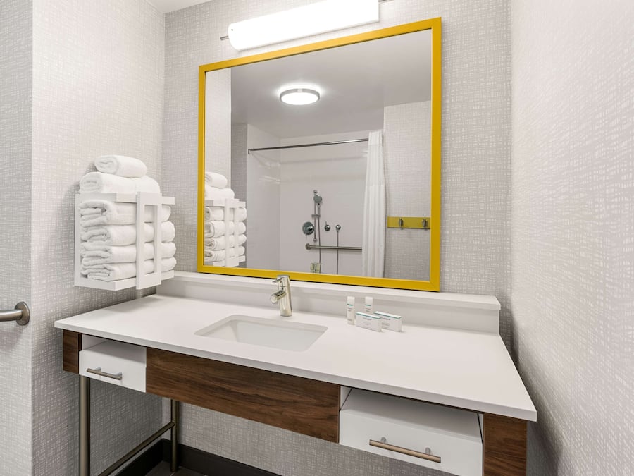 A modern bathroom with a white sink, a mirror with a yellow frame, and a towel rack with neatly folded towels.