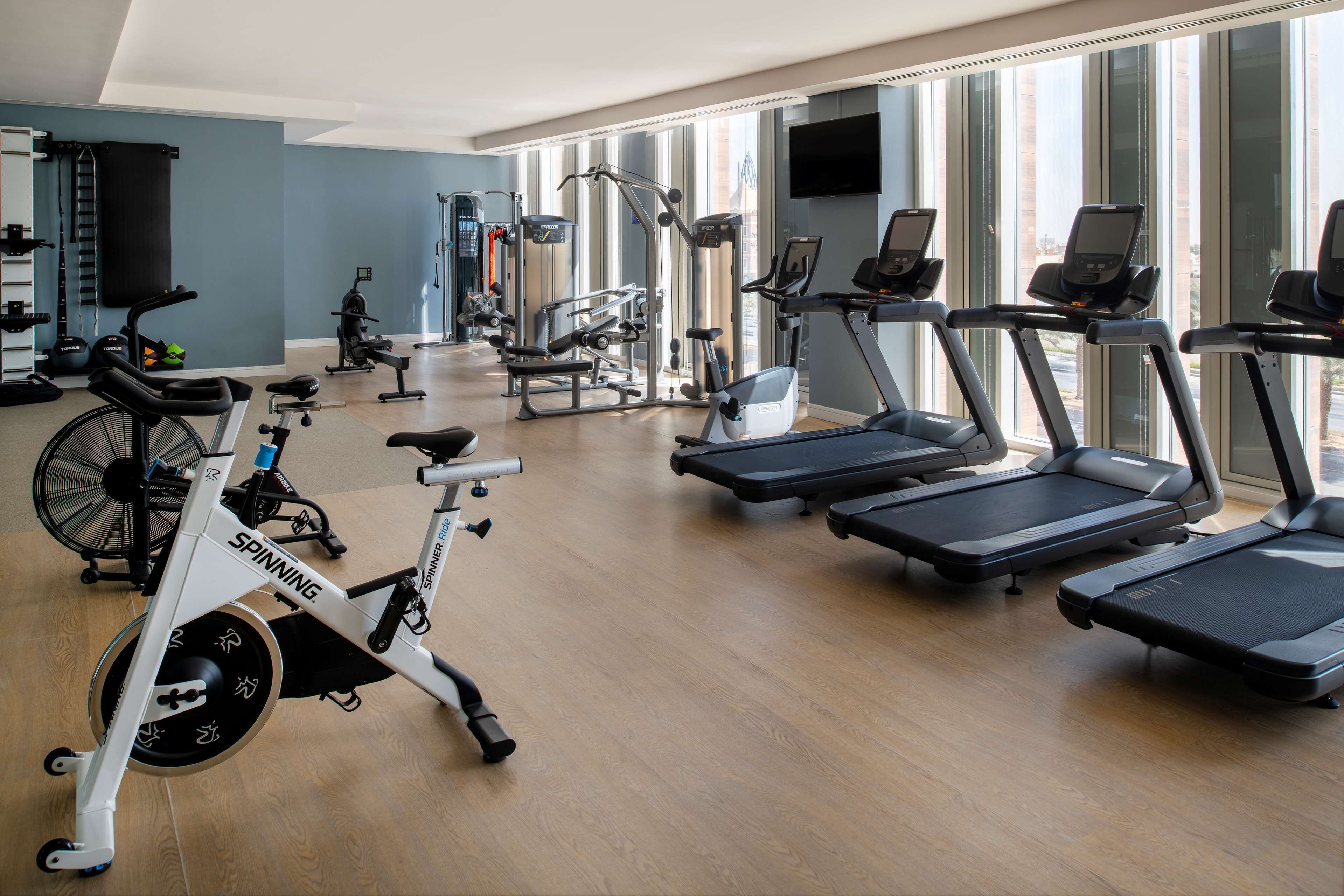 A gym with cardio machines, weight equipment, and a large window providing natural light.