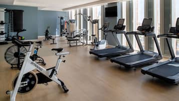 A gym with cardio machines, weight equipment, and a large window providing natural light.