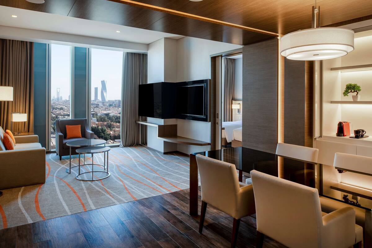 Ein modernes Hotelzimmer mit großem Fernseher, bequemen Sitzgelegenheiten, einer Essecke und Blick auf die Stadt.
