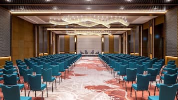 Un salón de conferencias con filas de sillas azules, una alfombra estampada y una lámpara moderna.