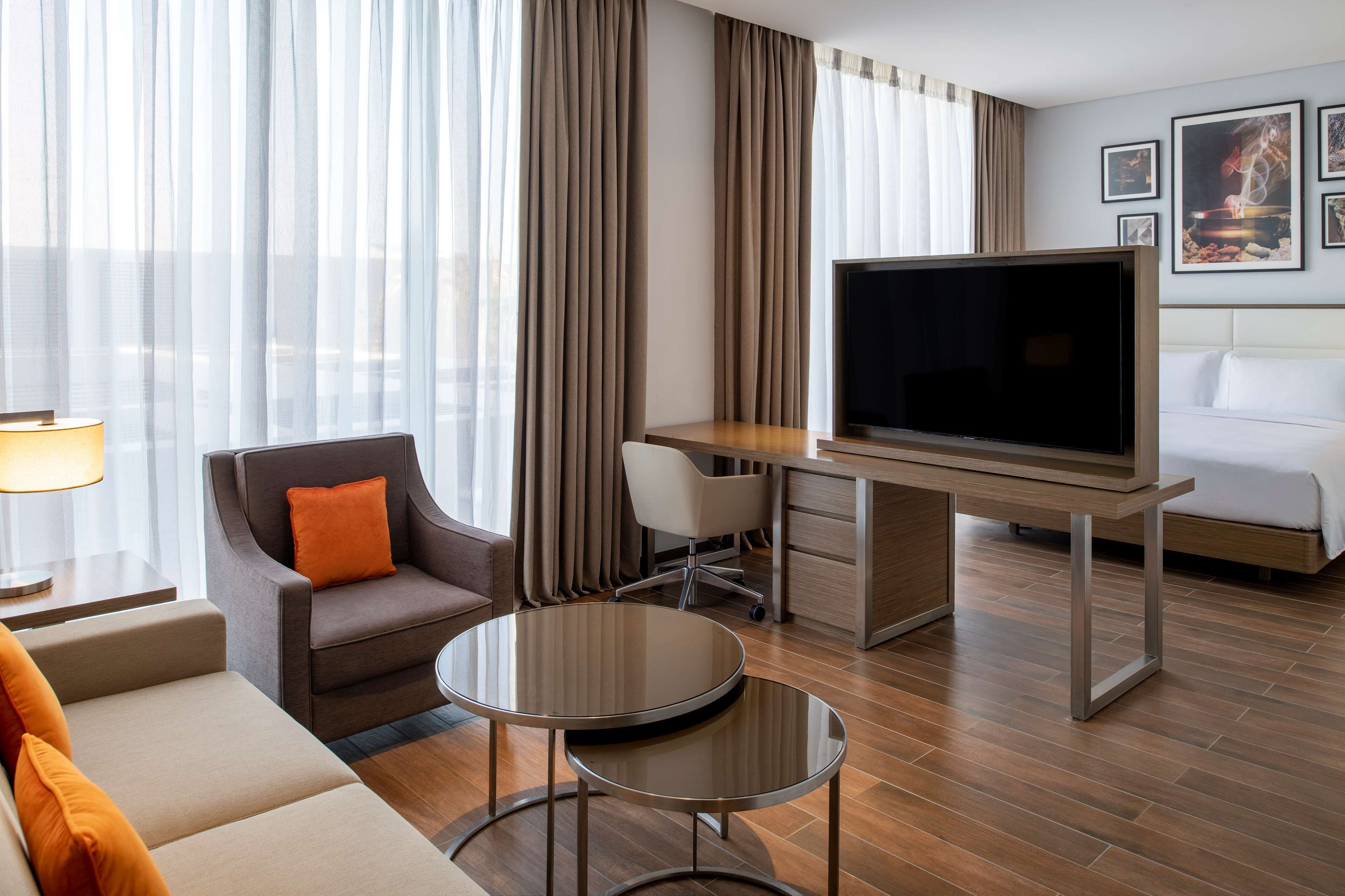 A hotel room with a bed, a desk with a TV, a chair, a sofa, and a small table.