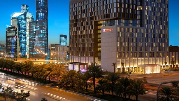 A modern hotel with a prominent Hilton Garden Inn sign, surrounded by high-rise buildings and palm trees. - Hilton Garden Inn Riyadh Financial District (Riyadh)