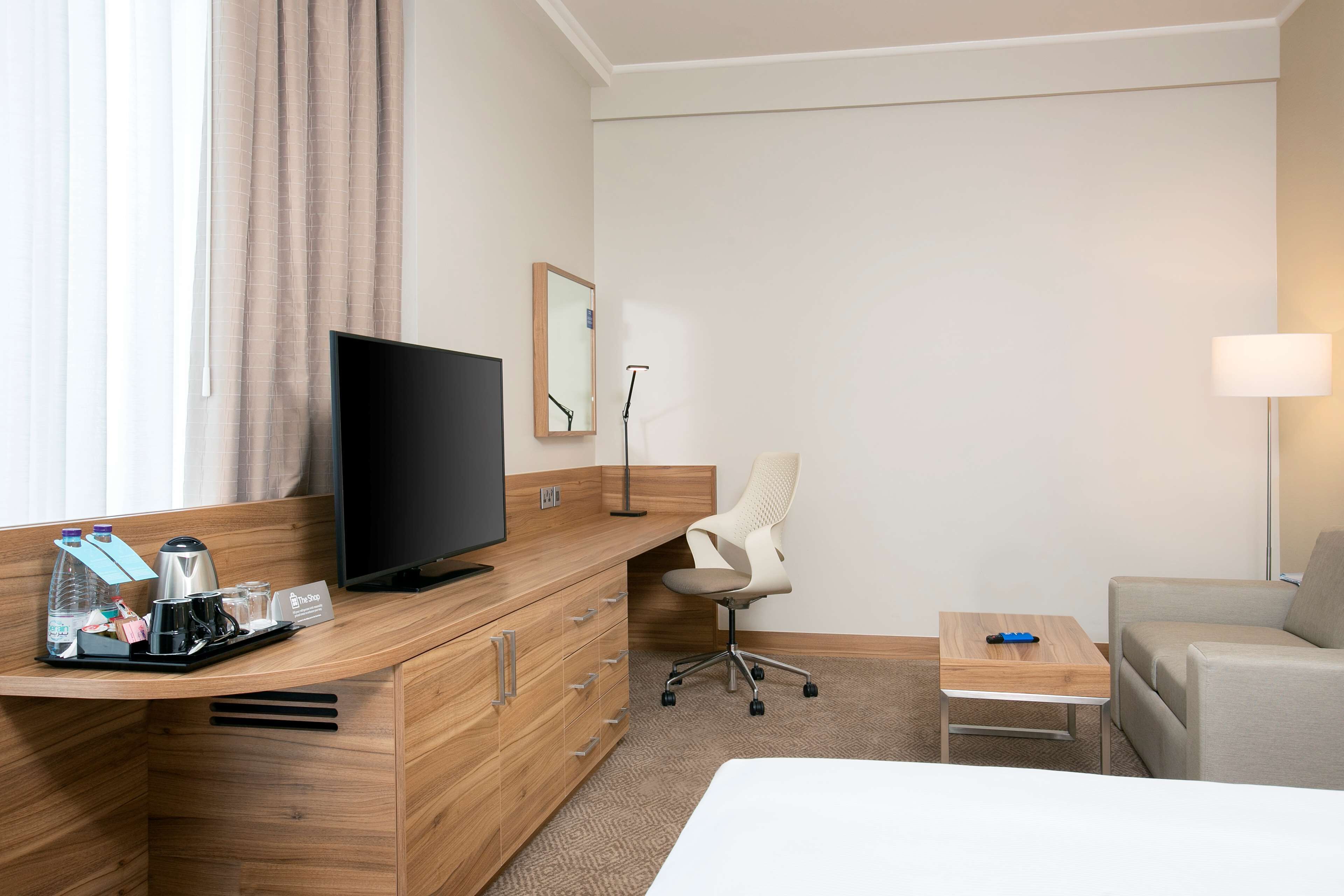Ett hotellrum med ett skrivbord i trä, en tv, en stol, ett litet bord och en säng.