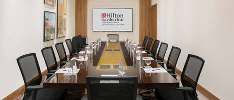 A conference room with a long table, black chairs, and a screen displaying the Hilton Garden Inn logo.