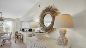 Une cuisine moderne avec des meubles blancs, un coin repas doté de chaises en osier et un grand miroir décoratif au mur.