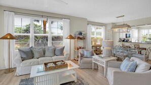 Un salon spacieux avec un canapé blanc, une table basse et un coin repas comprenant une table et des chaises en verre.