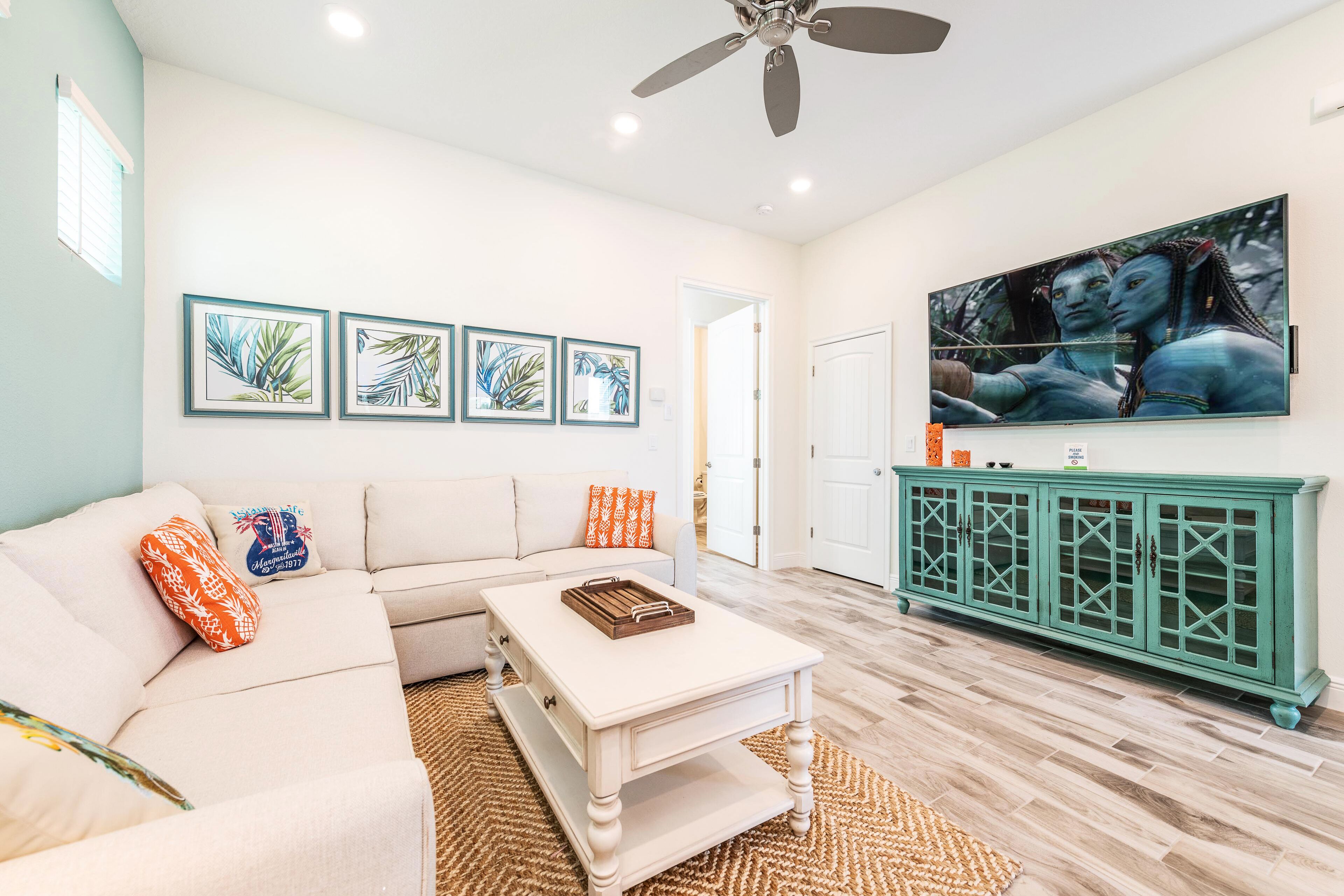 A living room with a white sofa, a coffee table, and a green cabinet. There are framed pictures on the wall and a large painting above the cabinet.