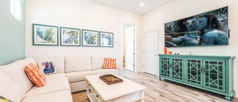 A living room with a white sofa, a coffee table, and a green cabinet. There are framed pictures on the wall and a large painting above the cabinet.