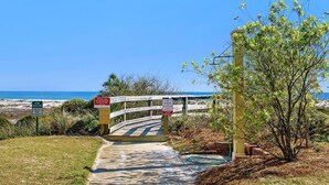 Un sendero que conduce a una zona de playa con señales de advertencia sobre la restauración de las dunas y la instrucción de retirar todos los objetos de la playa a diario.