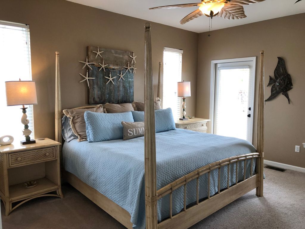 Una cama con dosel y un edredón azul, decoración de paredes con forma de estrella de mar y un ventilador de techo.