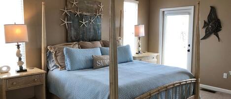 Una cama con dosel y un edredón azul, decoración de paredes con forma de estrella de mar y un ventilador de techo.